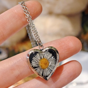 Detailed close-up of a heart-shaped locket necklace with real white daisy flowers in silver