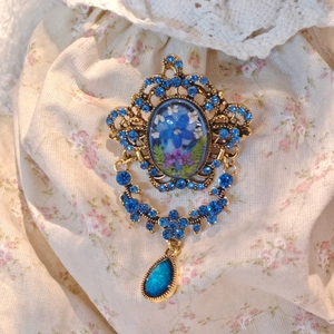 Detail of vintage gold brooch with blue pressed flower and hanging crystal teardrop