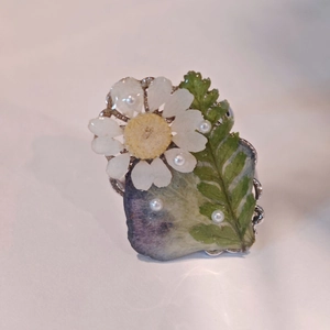 Macro view of handmade resin ring with real daisy flowers and pearl edge detail
