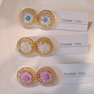 Detailed view of handmade daisy earrings set with woven gold metal frames on display cards