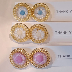 Detail of three handmade daisy resin stud earrings in blue yellow and purple colors