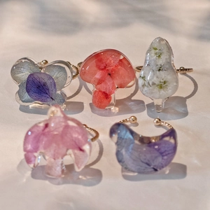 Détails macro de cinq bagues artisanales en résine avec fleurs séchées et anneaux dorés