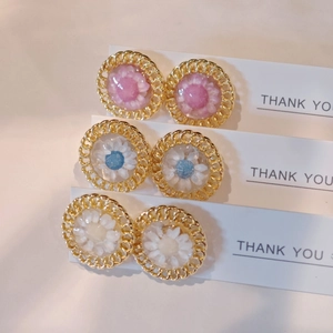Detailed macro of three pairs of resin daisy earrings with dried flowers in gold frames