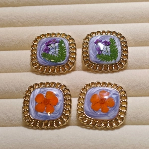 Macro shot of handmade square resin earrings with real dried flowers and gold metal borders