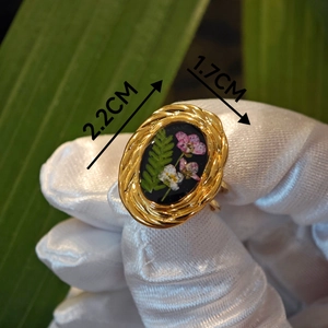 Detailed macro view of vintage oval resin ring with dried botanical flowers and fern