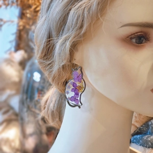 Detail of cat shaped earrings with purple dried flowers inside transparent resin