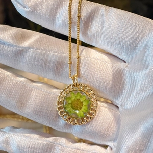 Detailed close-up of a resin pendant with an embedded green dried flower and gold border