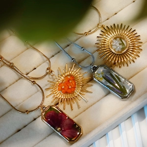 Detailed view of dried flower resin pendants in gold and silver frames on beige velvet