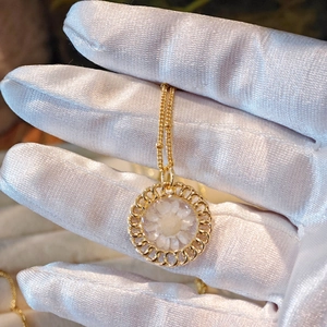 Detailed macro view of a gold braided round pendant featuring white dried flowers inside