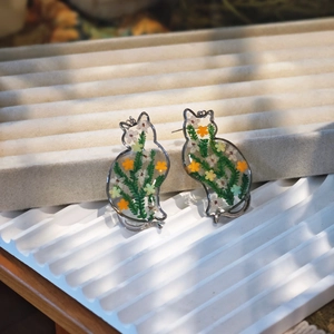 Macro detail of handmade cat earrings featuring real dried flowers in clear resin