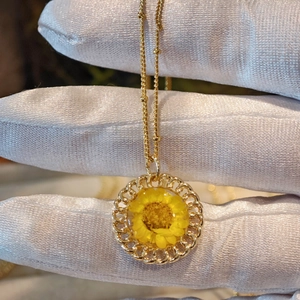 Detailed close-up of a golden necklace featuring a round pendant with yellow dried flowers