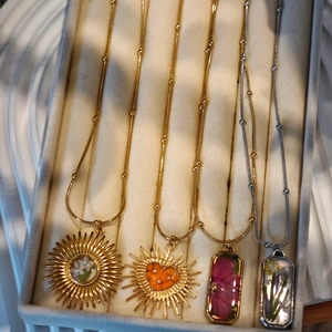 Close-up of four handmade pressed flower pendants with real botanicals in gold and silver
