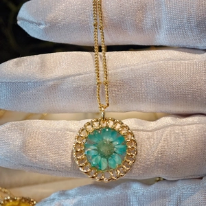 Macro detail of a golden necklace featuring a turquoise dried flower in a round pendant