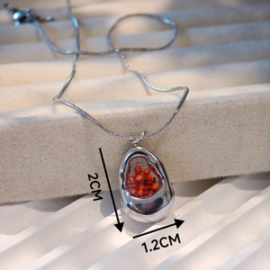 Detailed view of silver organic-shaped necklace with real red seeds inside a glass pendant