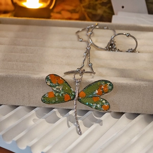 Detailed view of dragonfly pendant necklace with green and orange floral wings