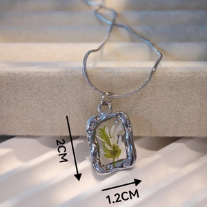 Macro view of handmade silver rectangle pendant with real white flowers and green leaves
