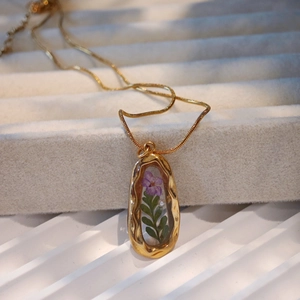 Vintage gold necklace with purple dried flower and leaf pendant in resin on white velvet