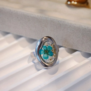 Detail of handmade stainless steel ring with blue dried flower in clear resin