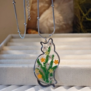 Detailed close-up of a cat-shaped resin necklace featuring yellow and white dried flowers