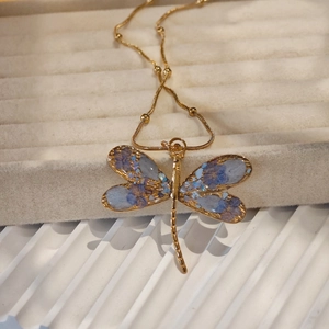 Close-up of golden dragonfly pendant with blue floral wings and gold chain necklace