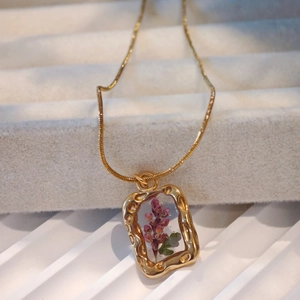 Macro shot of gold necklace featuring purple dried flowers in a textured resin pendant