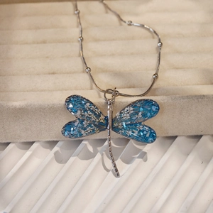 Macro shot of dragonfly pendant with blue resin wings and white petals on silver chain