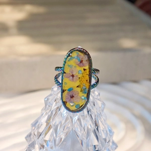 Makroaufnahme eines handgefertigten Harzrings mit Trockenblumen und Regenbogen-Edelstahl