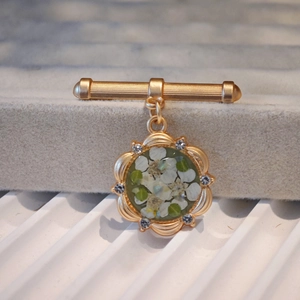 Close-up of vintage gold brooch with real white dried flowers and blue rhinestones