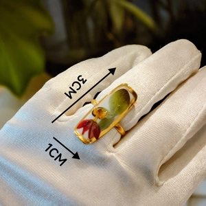 Detail view of gold ring with 3cm x 1cm rectangular floral enamel inlay and red flower