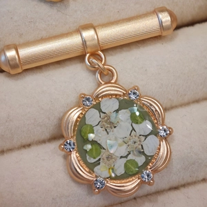 Detail of vintage resin brooch with dried flowers, green leaves and gold wavy frame