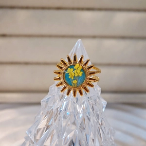 Macro detail of sun-shaped golden ring with real dried yellow flowers on blue base
