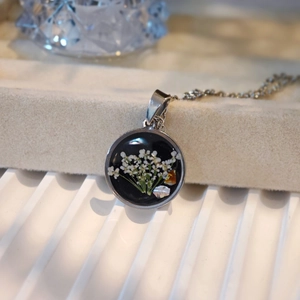 Macro shot of circular resin pendant with white dried flowers on stainless steel chain