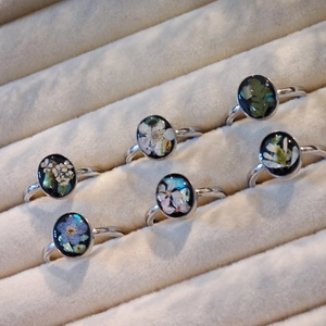 Detailed view of six handmade silver rings with real dried flowers and black resin inlays