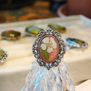Macro shot of handmade ring featuring real white dried flowers in resin with lace silver border