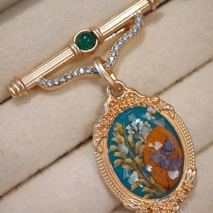 Detail of vintage gold brooch featuring dried flower specimen and emerald gemstone