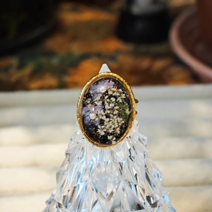 Primer plano de un anillo ovalado de resina con flores secas y perlas incrustadas