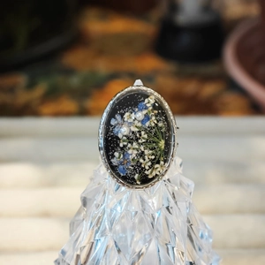 Detalle de un anillo ovalado con flores secas azules y perlas sobre resina negra