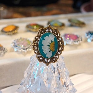 Macro shot of vintage bronze lace ring featuring a real white daisy flower in teal resin