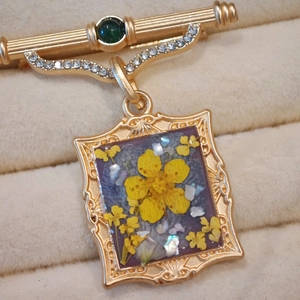 Macro shot of vintage brooch featuring real yellow flowers and green gem inlay