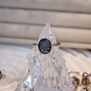 Detail of handmade resin ring with real blue dried flower on a black background