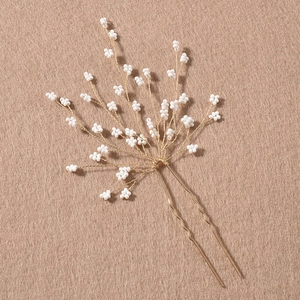 Épingle à cheveux artisanale avec fils dorés et perles blanches sur fond neutre