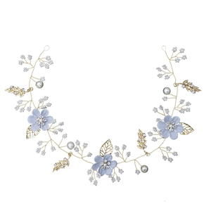 Détail de fleurs en tissu bleu et feuilles en métal doré sur un bandeau de mariée
