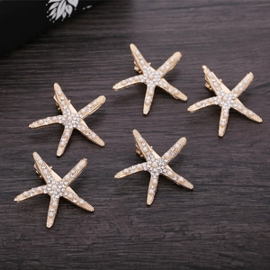 Set of 5 golden starfish hair clips with white rhinestones and pearls on wood background