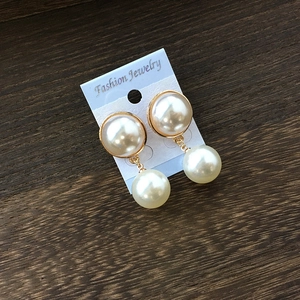 Boucles d'oreilles perles dorées de mariée sur carte à bijoux blanche et fond en bois sombre