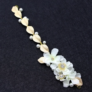 Détail d'un accessoire de mariée avec fleurs en tissu blanc et feuilles dorées