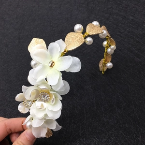 Détail de fleurs en tissu blanc avec feuilles en métal doré et perles sur le bandeau