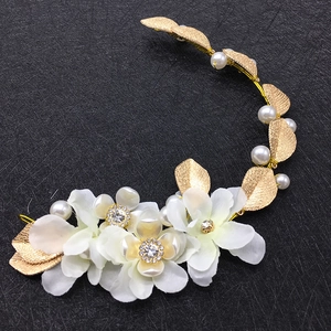 Détail d'un bandeau de mariée fait main avec des fleurs en tissu blanc et des feuilles dorées