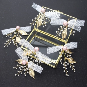Detailed close-up of bridal hairpins with white lace bows and pink pearls in a gold box