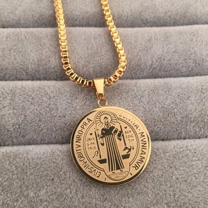 Macro shot of gold St. Benedict medal pendant with box chain on grey jewelry box
