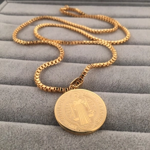 Detail of gold box chain necklace featuring a St. Benedict medal on a gray display